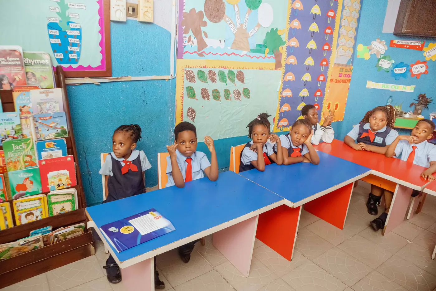 Nursery pupils at their colourful desks in a bright classroom lined with picture books