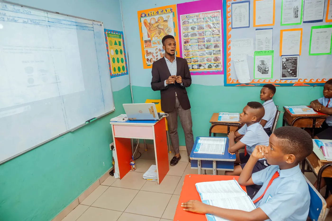 A primary teacher at the whiteboard with pupils at their desks